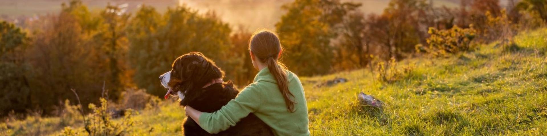 woman and a dog sitting beside each other on a hill