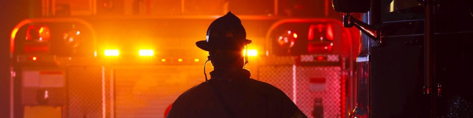 Front of fire truck with lights shining bright and a firefighter in front
